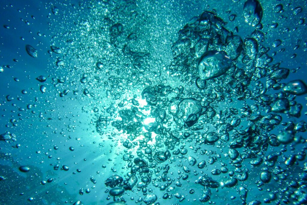 Capture of underwater bubbles rising towards the surface with sunlight streaming through.