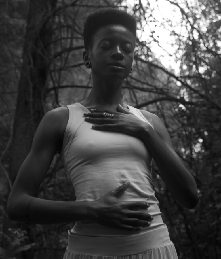 Black and white photo of a woman meditating in a serene forest, eyes closed.
